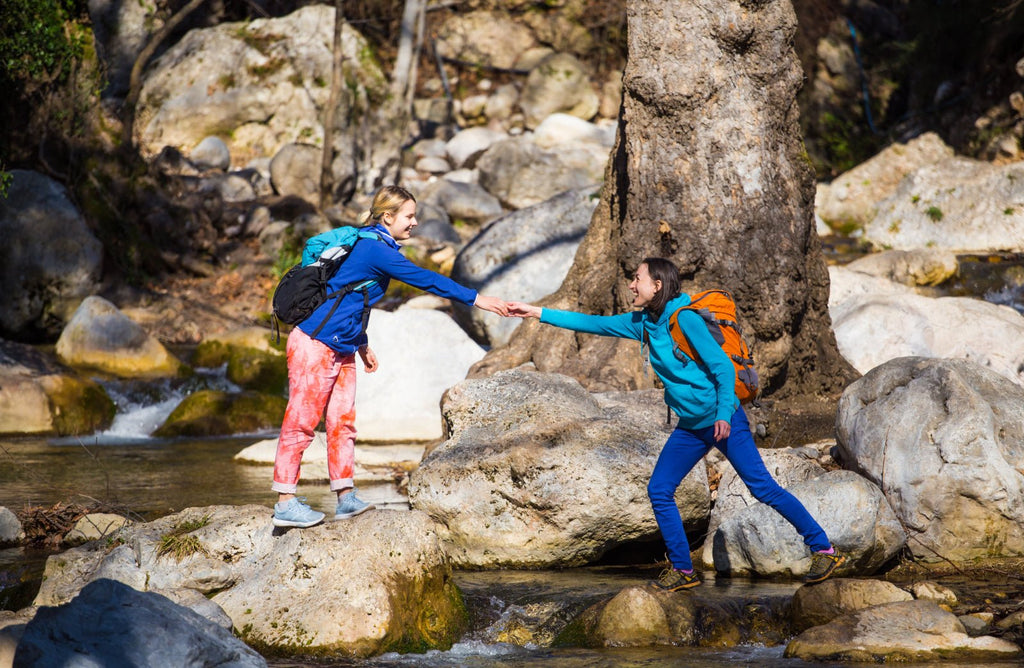 Two friends helping each other when hiking across a river
