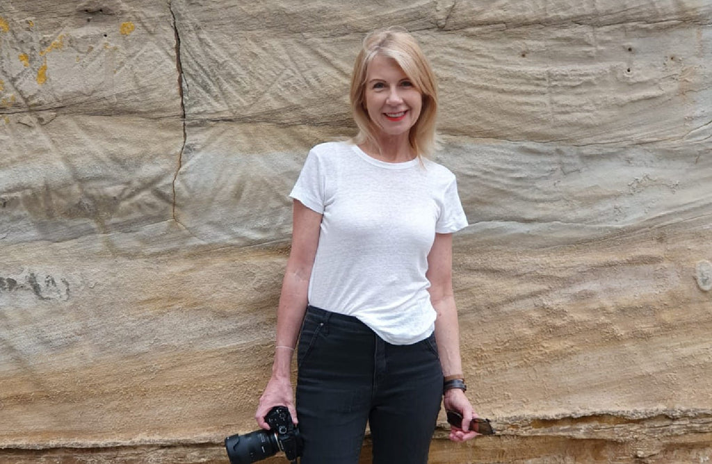 Sue standing in front of a rock, holding a camera